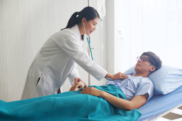 Female doctor is measuring the pulse of asian patient male who is lying in bed.